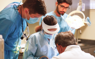 a female dentist is checking her patient, surrounded by other doctors